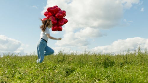 Woman Running on the Grass Field While Holding a Balloons