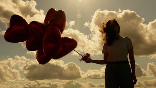 Woman with Bunch of Heart Shaped Balloons Standing Against the Sun