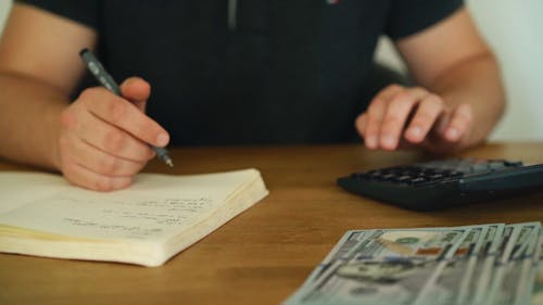 A Person Using a Calculator and Taking Notes