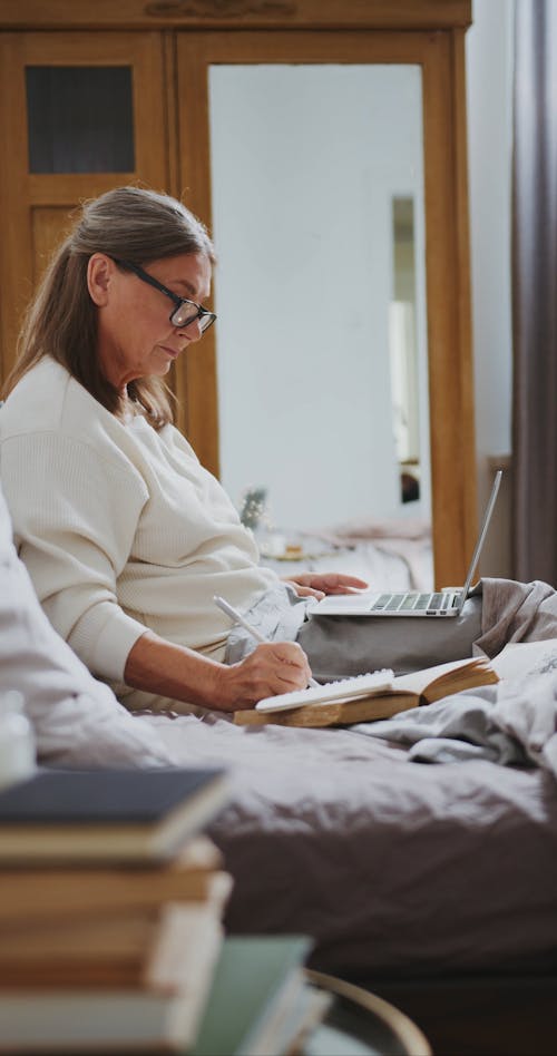 Woman Sitting on Her Bed While Using Her Laptop