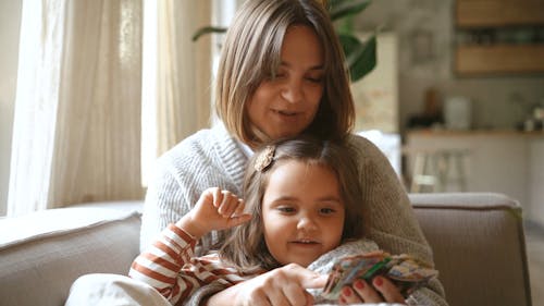 Cheerful Daughter Sitting on Mother's Lap Looking at Cards