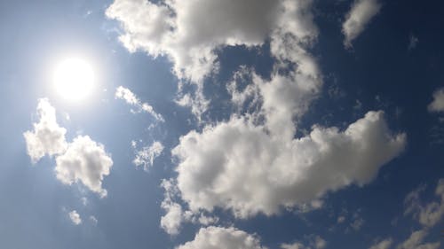 Sun and White Fluffy Clouds in Clear Blue Sky