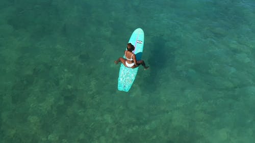 A Woman Sitting on Her Surfboard on Sea
