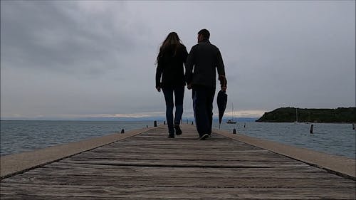 Back View of Couple Walking on Pier Holding Hands