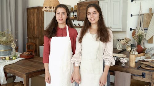 Twin Sister Standing In The Kitchen Wearing An Apron