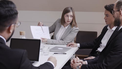 A Woman Presenting A Chart To A Group Of Businessmen