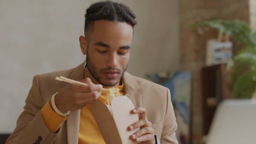 A Young Man Eating A Noodle Dish From A Box