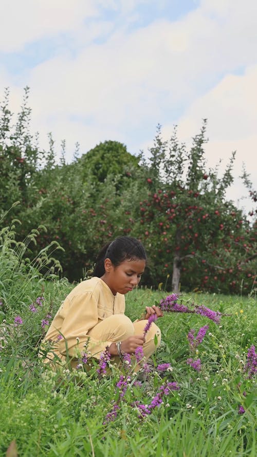 A Teenage Girl Picking Wild Flower From The Grass