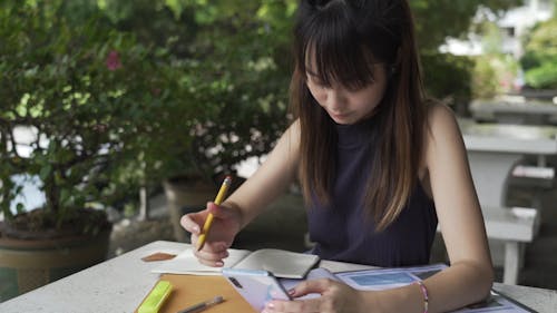 A Woman Using Her Smartphone While Writing on Her Notebook