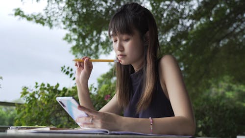 A Woman Studying and Writing While Using Her Smartphone