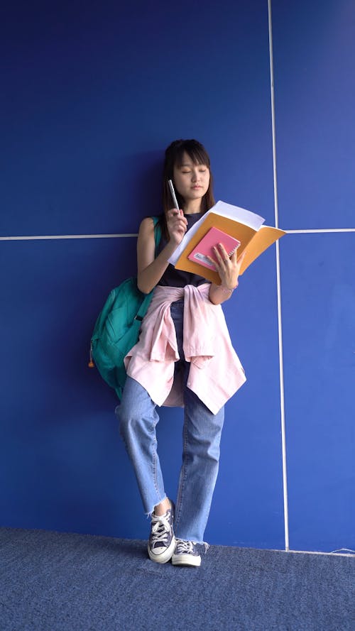 A Woman Reading Her Notes While Standing Near a Blue Wall