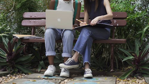 Two Students Sitting on a Bench While Discussing Their Notes