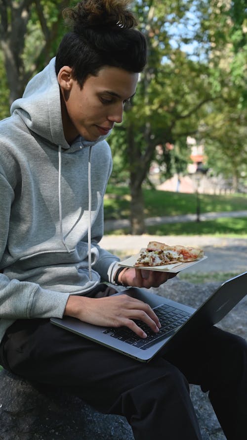 Man Busy Using His Laptop while Holding a Pizza