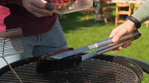 Person Putting Grilled Meat on a Plate