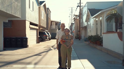 An Elderly Couple Standing In The Middle Of The Street