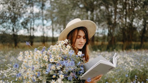 A Woman Reading A Book With Flowers On Hand