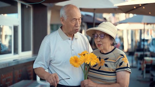 Elderly Couple Standing on the Street Side Holding Yellow Flowers
