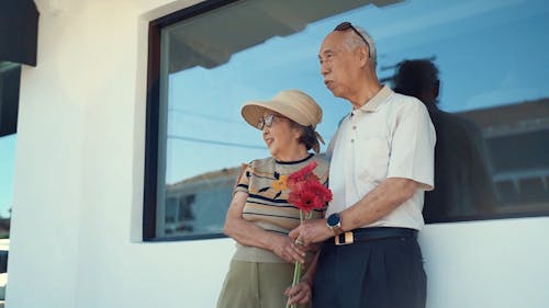 An Elderly Man Holding A Bouquet Of Flowers Beside Her Wife