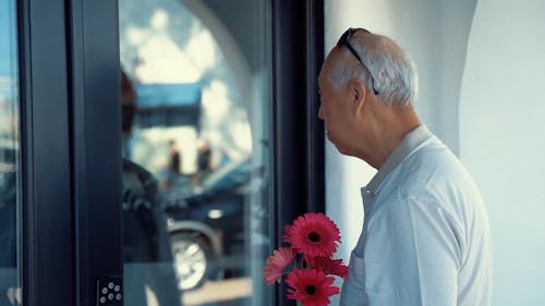 Elderly Man Holding Flowers In Front of The Door