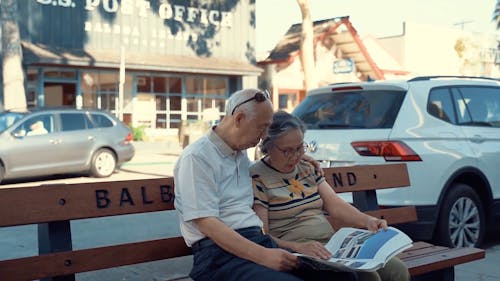 Elderly Couple Sitting on the Bench Reading Newspaper
