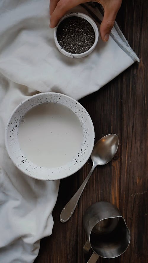 A Person Pouring Chia Seeds in a Bowl With Almond Milk