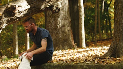 A Man Smoking a Cigarette While Petting His White Dog