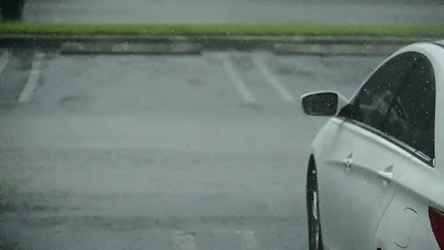 A White Car Parked in a Parking Lot While Raining