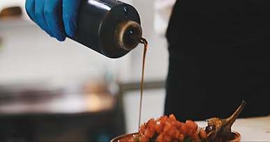 a person pouring a black sauce on a side dish food