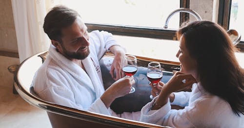 A Couple Drinking Red Wine In A Bath Tub