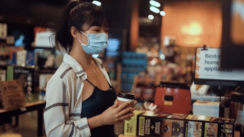 Woman Holding a Cup While Walking Inside a Store
