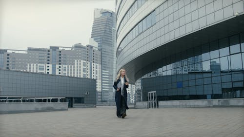 A Woman Walking Outdoors Holding A Coffee And Laptop