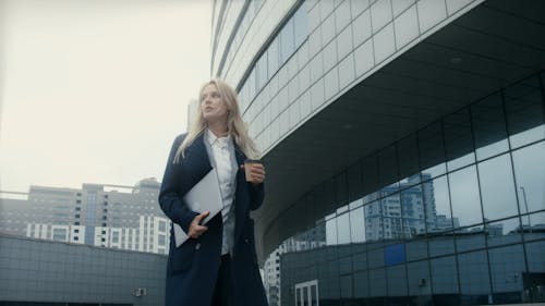 A Woman Walking Outside Holding A Laptop And Coffee