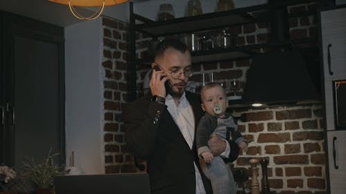 A Man is Talking on the Phone While Carrying a Baby with Pacifier 