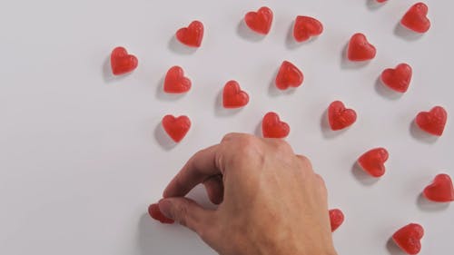 Close-Up View of a Person Putting Red Hearts on White Surface