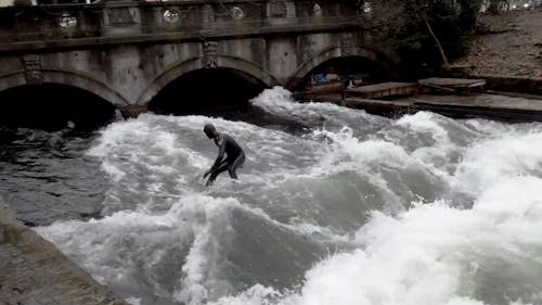 Person Surfing in Black Suit at a Canal