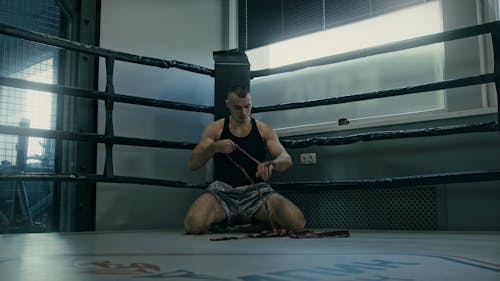 Man Sitting on a Boxing Ring While Putting His Hand Wraps 