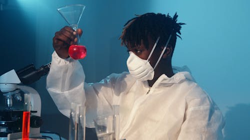 A Man Doing an Experiment While Looking at a Flask With Red Liquid