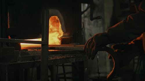 A Blacksmith Looking at Metal Rods inside a Furnace