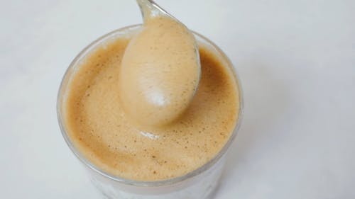 Person Holding Silver Spoon Mixing Brown Liquid in a Glass