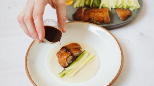 Person Pouring Brown Sauce on Sliced Meat on White Ceramic Plate