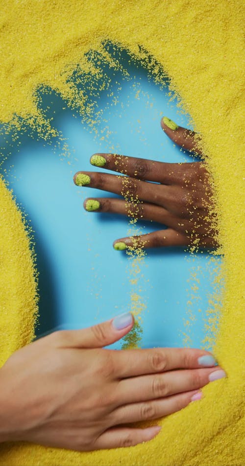 A Person Wiping a Yellow Glitters while Showing a Hand with Nail Polish