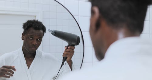 A Man Looking at the Mirror while Using Hairdryer