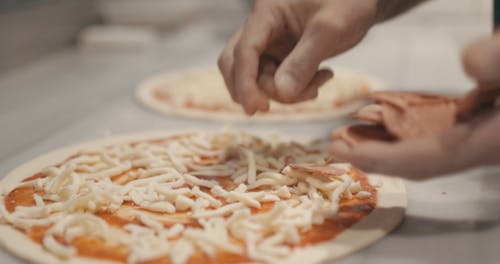 Person Putting Pepperoni Toppings on the Top of a Pizza