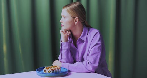 A Person in Lilac Shirt in Front of a Plate of Sushis