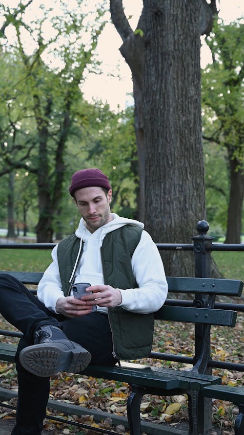 Man Using Smartphone While Sitting in a Park Bench
