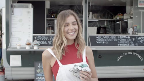 Blonde Woman Eating a Burger In Front of a Food Truck