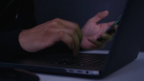 A Person Typing on a Laptop while Holding a Phone