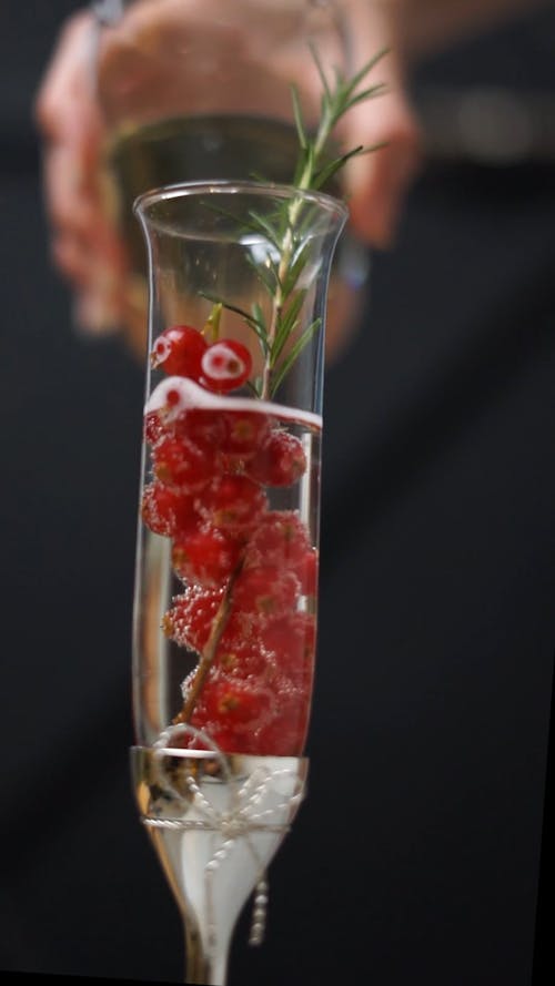 Person Adding Champagne to a Glass with Berries and Rosemary