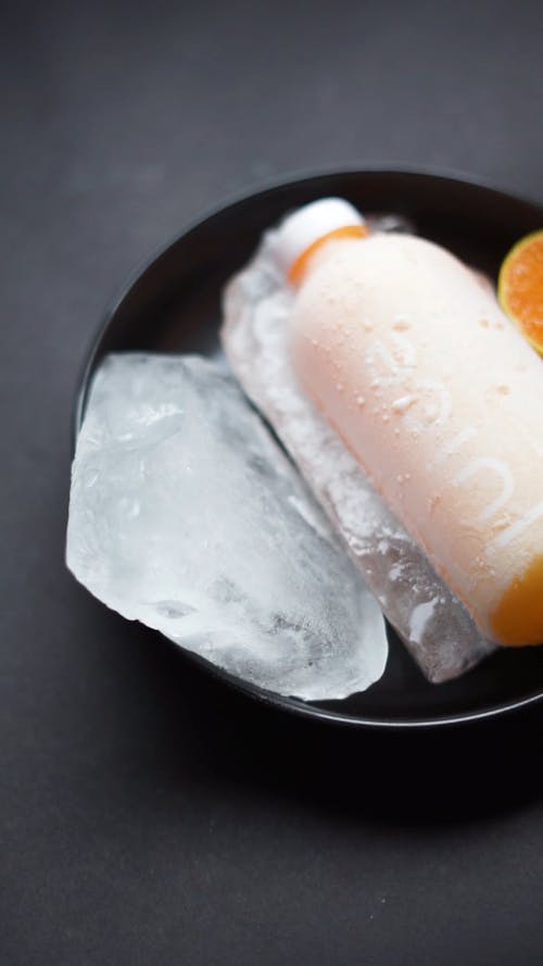 A Person Putting a Sliced Orange Beside an Ice and a Bottle of Juice