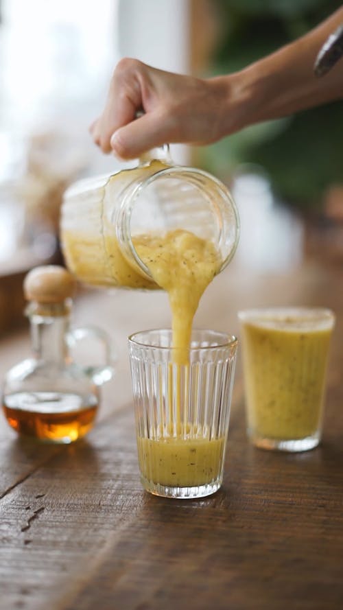 Person Pouring Smoothie on a Drinking Glass